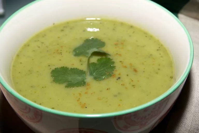 Watercress soup with a sprig of coriander as garnish in a white bowl with green trim