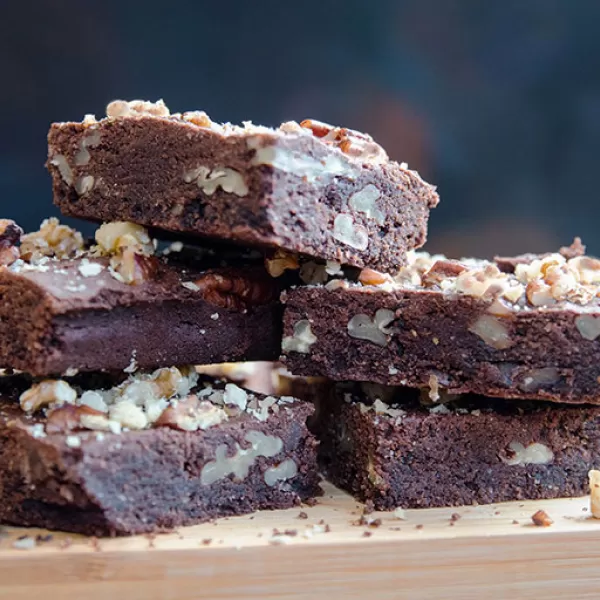 A stack of chocolate and pecan brownies, sprinkled with pecan crumbs and crushed walnut, fresh out of the oven